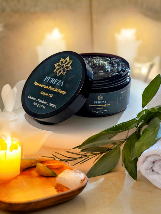 PUREZA Moroccan Black Soap with olive leaves and candles on a blurred background