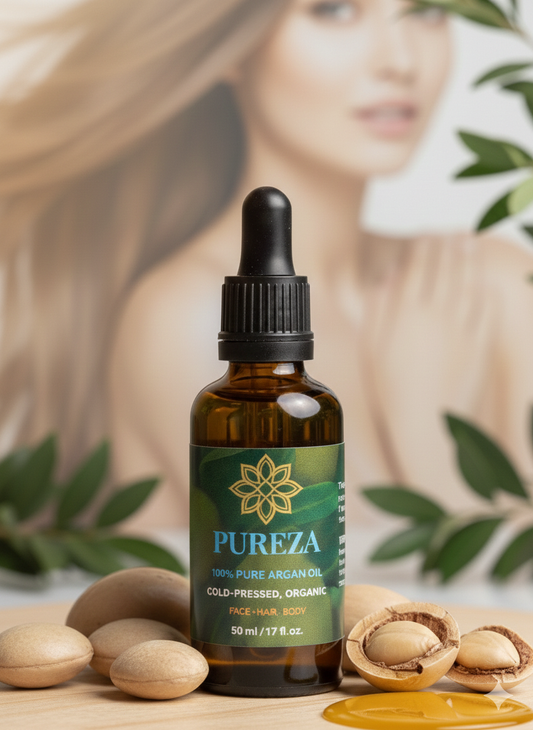 A bottle of Pureza Cold-Pressed Organic Face, Hair, and Body Oil with a black dropper cap, styled with argan nuts and leaves on a wooden surface, with a blurred model in the background.
