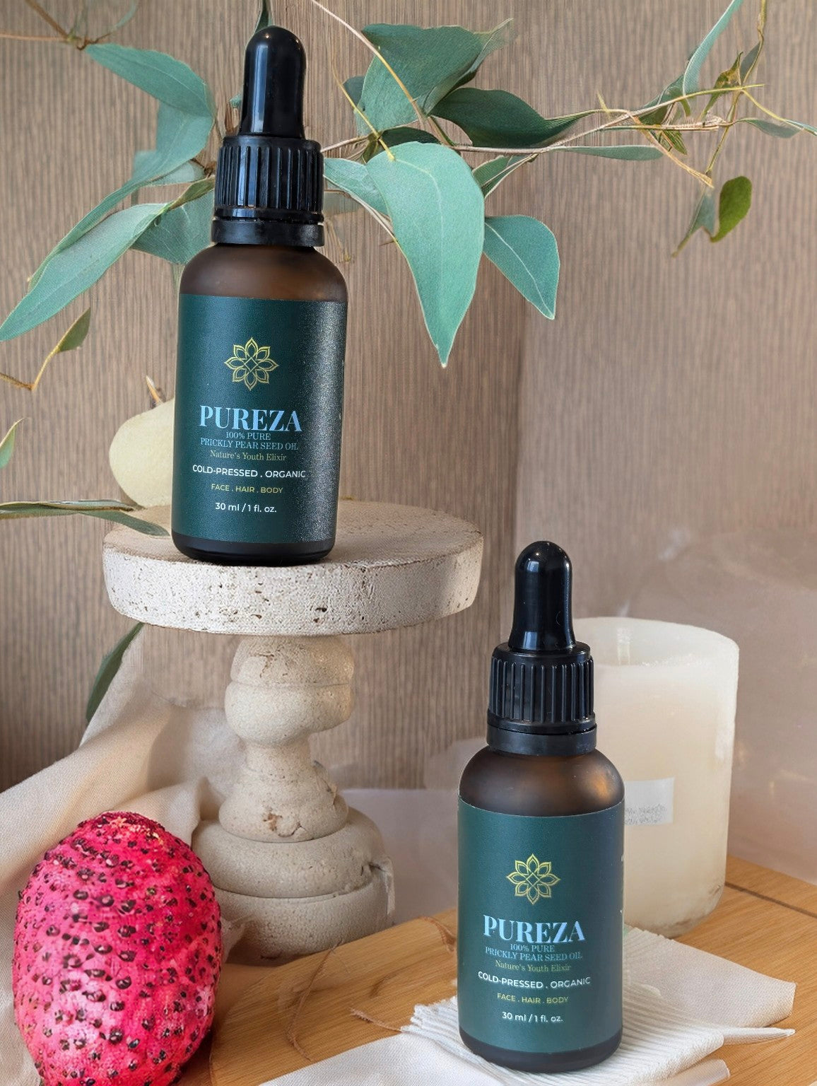 PUREZA prickly pear oil bottle with dropper on a wooden surface with eucalyptus leaves and dragon fruit.